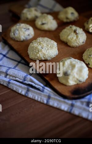 On the board prepared for frying Russian traditional home-made cottage cheese pancakes with raisins - cheesecakes on a wooden table. Stock Photo