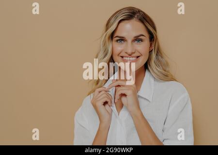 Young beautiful positive female with blond dyed hair touching lips with finger and smiling at camera Stock Photo