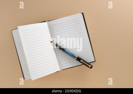 Open lined notebook with old fountain pen isolated on light brown background in top view, flat lay, copy space Stock Photo