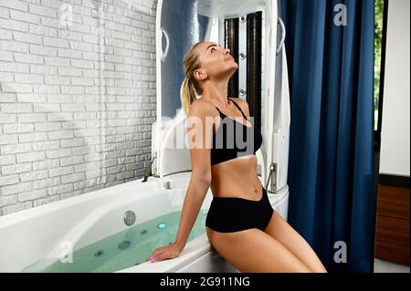 Pretty woman with perfect skin getting ready for spa beauty therapy in spa capsule. Hydro and vibromassage in a modern wellness spa Stock Photo