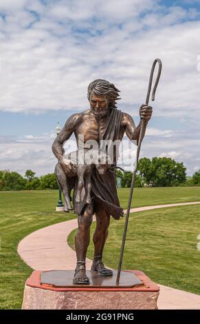 Sioux Falls, SD, USA - June 2, 2008: Closeup of bronze Saint Christopher with lamb and staff statue on pedestal set in green park near the falls under Stock Photo
