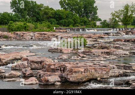 Sioux Falls, SD, USA - June 2, 2008: Focus on the cascade of waterfalls over beige rocks with some green foliage in back . Stock Photo
