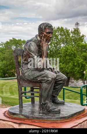 Sioux Falls, SD, USA - June 2, 2008: Closeup of thinking man on chair bronze statue in Falls Park under heavy gray sky with green foliage as backdrop. Stock Photo
