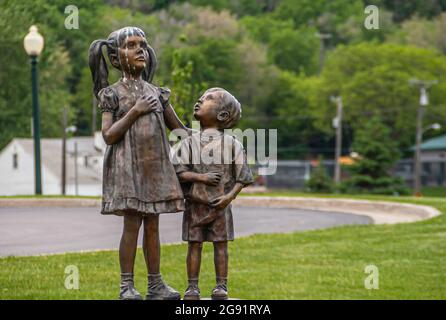 Sioux Falls, SD, USA - June 2, 2008: Closeup of Sister with little brother bronze statue in Falls Park with green foliage as backdrop. Brother looks i Stock Photo