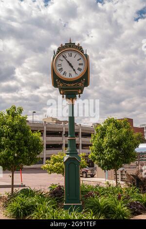 Sioux Falls, SD, USA - June 2, 2008: Green-golden circular city clock on decorative piller set in small green garden with parking garage as backdrop u Stock Photo