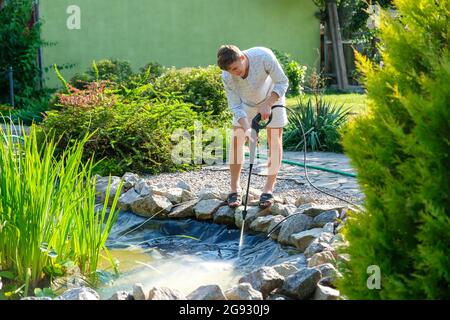 man cleans garden pond bottom with high-pressure washer from mud and sludge. Stock Photo