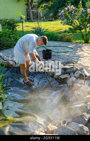 man cleans garden pond bottom with high-pressure washer from mud and sludge. Stock Photo