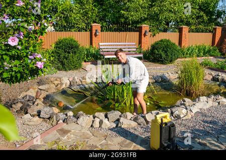 man cleans garden pond bottom with high-pressure washer from mud and sludge. Stock Photo