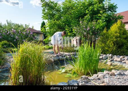 man cleans garden pond bottom with high-pressure washer from mud and sludge. Stock Photo