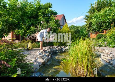 man cleans garden pond bottom with high-pressure washer from mud and sludge. Stock Photo