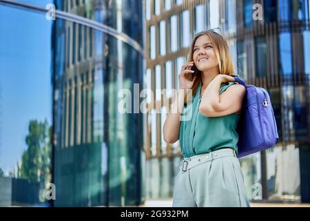 Cheerful slim woman talks with friend by phone outdoors. Stock Photo