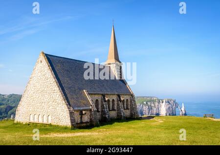 Rear view of Notre-Dame de la Garde on the Amont cliff in Etretat, Normandy, with the Aval cliff, its arch and the Needle in the distance. Stock Photo