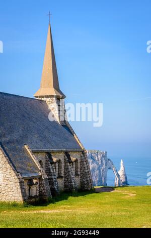 Rear view of Notre-Dame de la Garde on the Amont cliff in Etretat, Normandy, with the Aval cliff, its arch and the Needle in the distance. Stock Photo