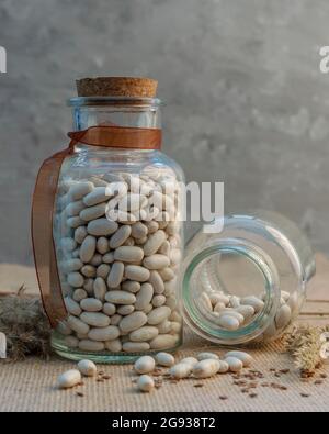 Dried white beans in two glass containers, one of which is open horizontally on the table Stock Photo