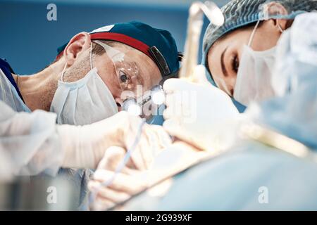 Operation view from a patient, a team of doctors bottom view doing the operation in modern equipment, lighting devices on the head Stock Photo
