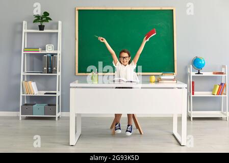 Funny schoolgirl in the eyes raised her hands up in the classroom. Stock Photo
