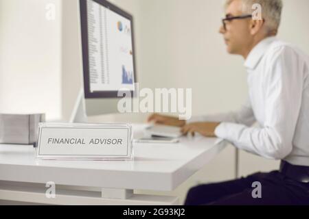 Nameplate that reads Financial Advisor with a man working on a computer in the background Stock Photo