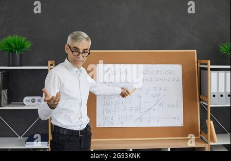 Portrait of senior teacher standing in front of classroom board during online class Stock Photo