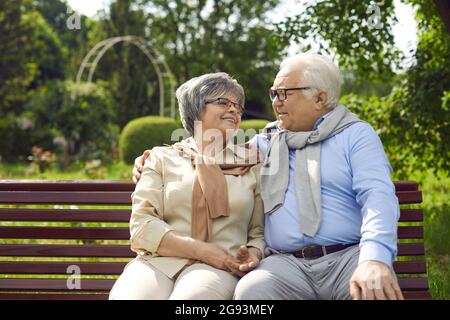 Happy loving senior couple sitting on bench and hugging looking into eyes Stock Photo