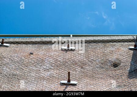 A stone wall standing by a road secured with a galvanized metal mesh against a blue sky, selective focus. Stock Photo