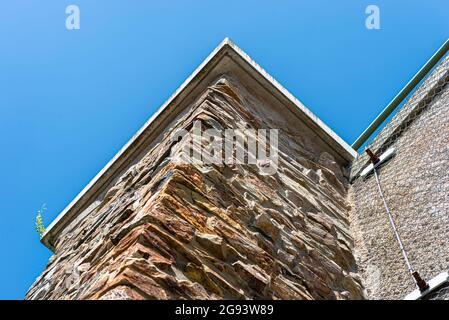 A stone wall standing by a road secured with a galvanized metal mesh against a blue sky, selective focus. Stock Photo