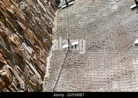 A stone wall standing by a road secured with a galvanized metal mesh, selective focus. Stock Photo