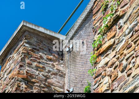 A stone wall standing by a road secured with a galvanized metal mesh against a blue sky, selective focus. Stock Photo