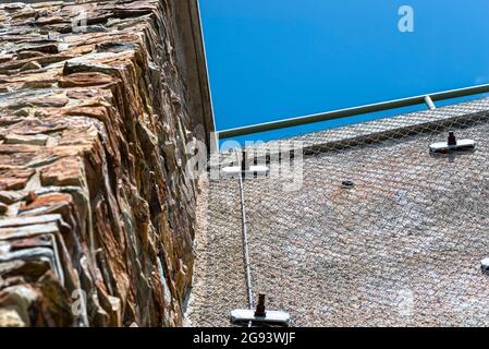 A stone wall standing by a road secured with a galvanized metal mesh against a blue sky, selective focus. Stock Photo