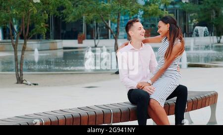 Young mixed-race family having nice time outdoors: laughing, hugging and talking to each other. The fountains are in the background. Stock Photo