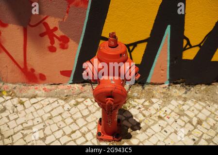SETUBAL, PORTUGAL - Jul 04, 2021: A hydrant in the street in front of a graffiti wall in Setubal, Portugal Stock Photo