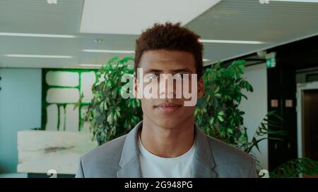 Young African-American man in elegant suit standing in modern office and smiling happily at camera. Stock Photo
