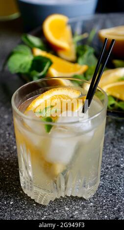 Lemon lemonade with mint and ice in a glass with black plastic tubes on a background of fruit. Cooling summer drink. Vertical close up Stock Photo
