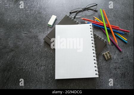 Creative office desk with a mock up spiral notebooks, colored pencils, glasses and supplies on a dark gray table, copy space, selected focus, narrow d Stock Photo
