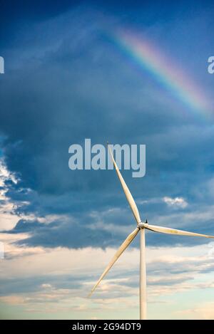 rainbow in a dark sky over a wind turbine Stock Photo
