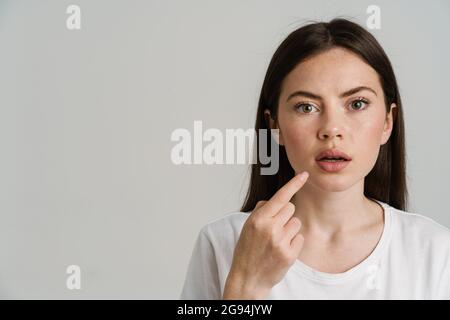 Surprised woman pointing finger at her mouth and looking at camera isolated over white background Stock Photo