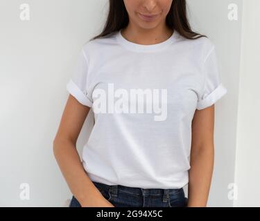 Tshirt mockup, front view of unrecognizable woman wearing white tshirt. Copy space on empty area on her t-shirt for design or inscription. Fashion lifestyle mock up of white tshirt. T-shirt template. Stock Photo