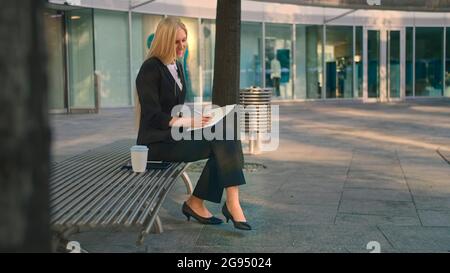 Side view of elegant businesswoman sitting on bench in patio and writing in notepad while working. Stock Photo