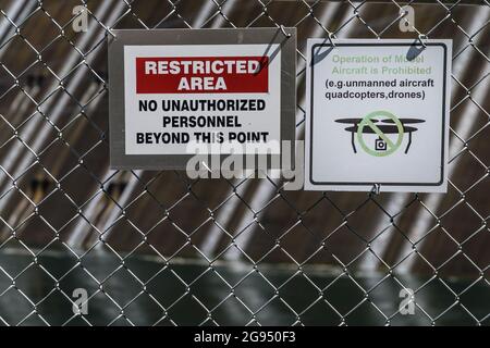 Signs on chain link fence reading 'Restricted Area' and no drone flying or unmanned aircraft. Stock Photo