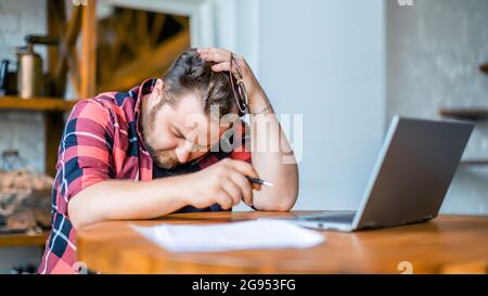 Photo of an exhausted man working at home before the deadline. Conceot of modern technologies in everyday life. Stock Photo