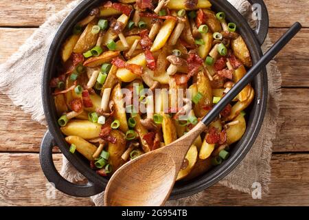 Rustic style fried potatoes with onions, mushrooms and bacon close-up in a frying pan. horizontal top view from above Stock Photo
