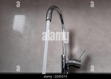 Horizontal view of the silver faucet in the bathroom. Water is flowing from the open tap. Interior of a modern bathroom with fittings. Stock Photo