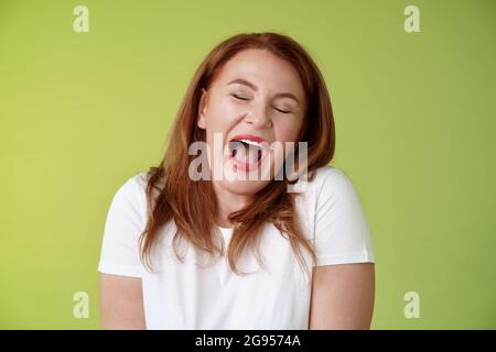 Lazy weekends finally time sleep. Cheerful redhead middle-aged 50s woman yawning satisfied close eyes feel sleepy wake up early morning wanna take nap Stock Photo