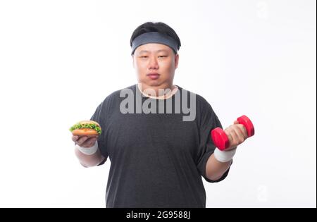 Young Asian funny fat sport man holding hamburger and dumbbell isolated on white background. Healthy lifestyle concept. Stock Photo