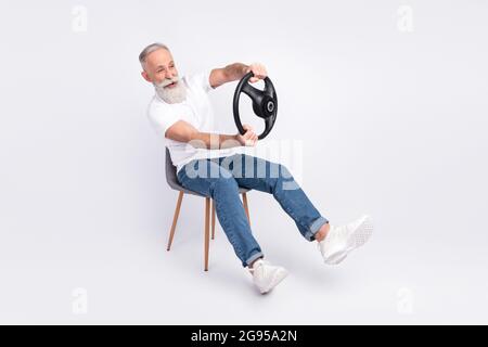 Portrait of nice cheerful man sitting on chair holding in hands steering wheel driving invisible car isolated over grey color background Stock Photo