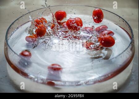 Antioxidant natural organic vegetable Fresh red baby cherry plum tomatos (baby tomato,cherry tomato) group dropping on the water bowl with water splas Stock Photo