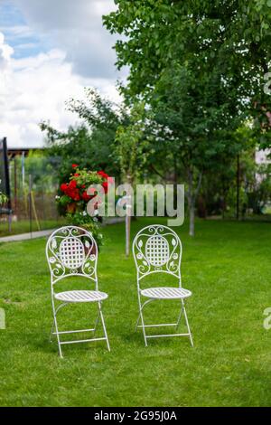 Two white painted metal chairs with beautiful carvings on the lawn in the garden Stock Photo