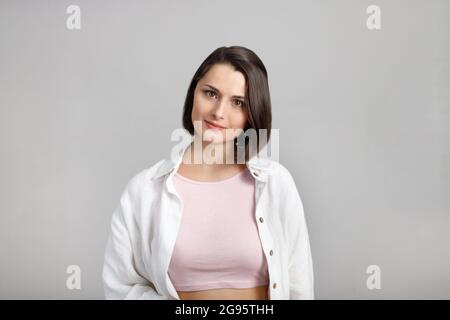 High key calm portrait of young brunette mixed race woman in pink tank and white shirt looking at camera. Stock Photo