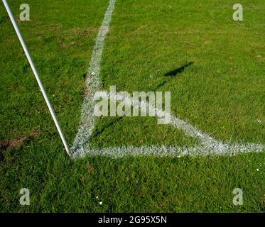 A  wonky amateur football pitch close up of the corner kick area newly painted and marked out with the shadow of the corner flag from the sun. Stock Photo