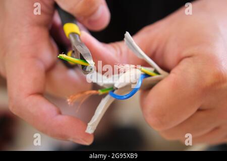 Close up of a young caucasian man hands peeling a wire using a plier to repair it. Stock Photo