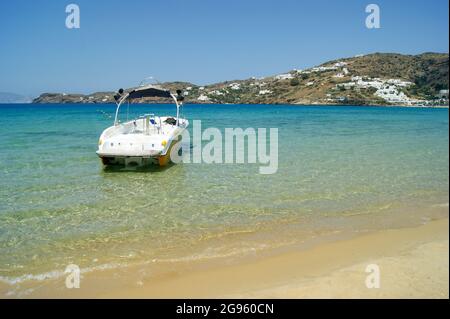 Ios island, Greece. Beautiful beach scene, with a small boat in the foreground, at Mylopotos bay. Crystal clear blue sea, clear sky.  Copy space. Stock Photo
